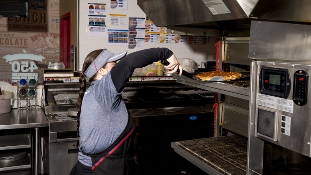 A worker takes a pizza out of the oven at a Domino's restaurant in Trenton, Michigan, US. Photographer: Nic Antaya/Bloomberg